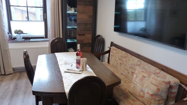 Un coin repas confortable avec un plateau en bois, des chaises et un canapé. Un grand téléviseur est accroché au mur.