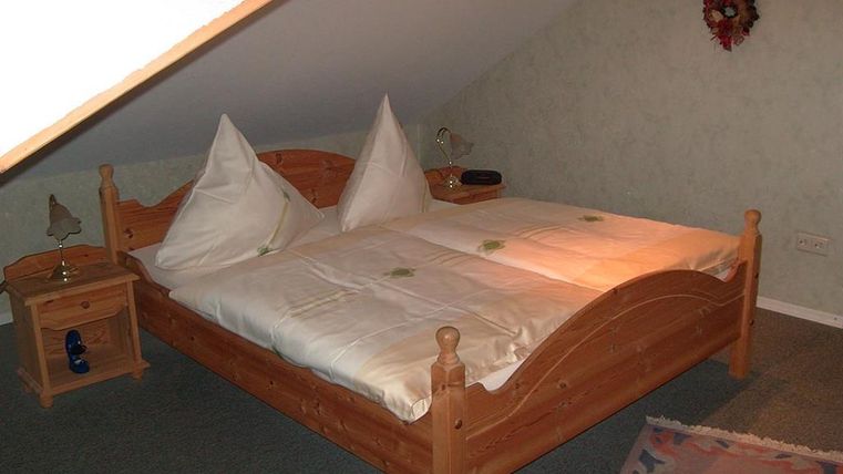 Ein gemütliches Schlafzimmer mit einem Holzbett und zwei dekorativen Kissen. Neben dem Bett steht ein Nachttisch mit einer Lampe.