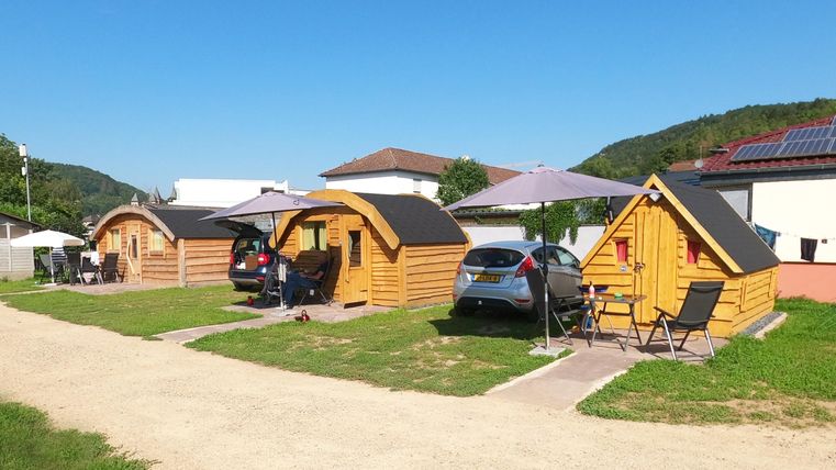 Deux chalets en bois confortables se trouvent sur un terrain bien entretenu. En arrière-plan, des voitures sont garées et un ciel bleu est visible.