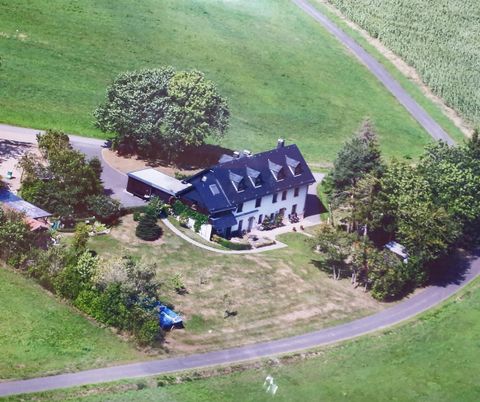 Une grande maison moderne entourée de prairies vertes et d'arbres. L'allée mène doucement au bâtiment, qui est entouré d'un terrain bien entretenu.
