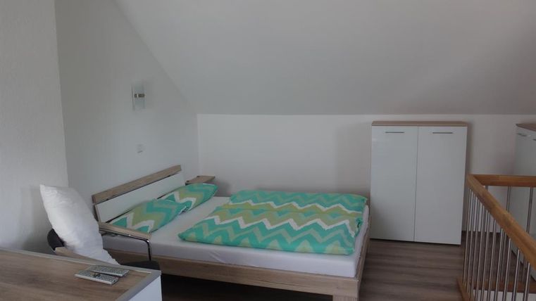 Une chambre simple avec un lit double et des couvertures colorées. Il y a des meubles modernes et une atmosphère lumineuse et accueillante.