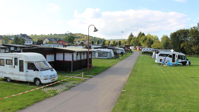 Een camping met verschillende campers en tenten. Het landschap is groen en er is een geplaveid pad tussen de standplaatsen.