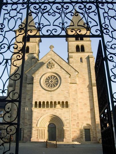 Une église impressionnante avec deux tours et un grand rose window. L'image montre l'entrée par une porte en fer forgé.