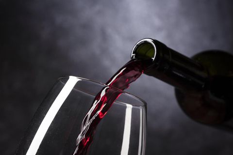 Eine Flasche Rotwein wird in ein Glas gegossen. Der Hintergrund ist dunkel und schlicht.