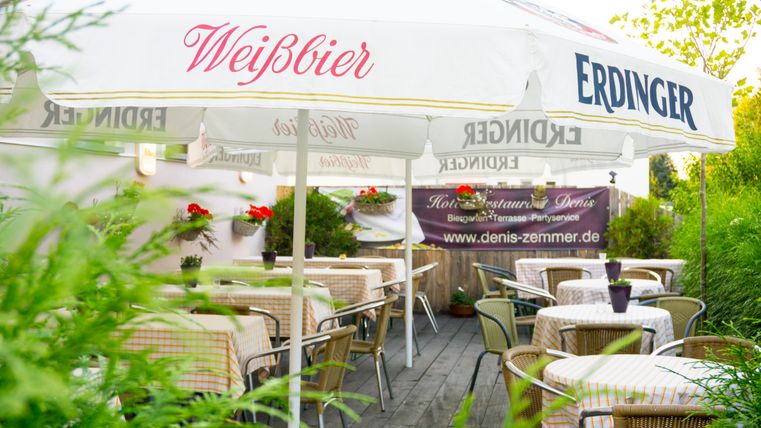 Un restaurant accueillant avec un espace extérieur et une terrasse en bois. Les tables sont dressées et décorées de fleurs, tandis que des parasols offrent de l'ombre.