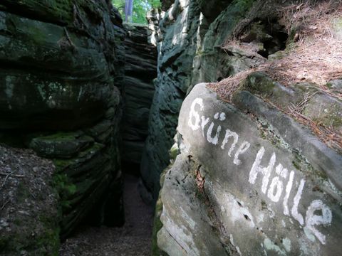 Eine enge Schlucht mit hohen Felsen, die von grünem Moos bedeckt sind. An einer Felswand steht die Aufschrift "Grüne Hölle".