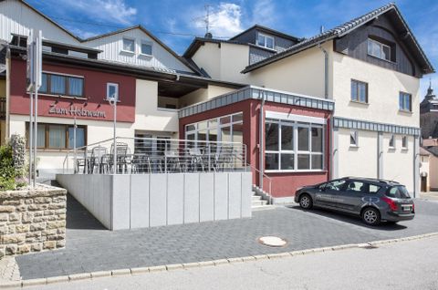 Ein modernes Gebäude mit einem einladenden Restaurant und einer Terrasse. Vor dem Haus steht ein Parkplatz mit einem Auto.