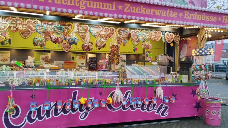 Ein bunter Süßigkeitenstand mit vielen Leckereien. Hier gibt es Herzchen, Zuckerwatte und weitere Snacks.