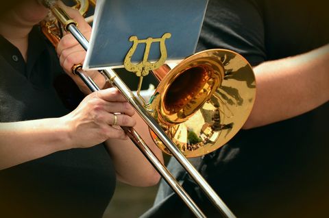 Eine Person spielt eine glänzende Posaune. Im Hintergrund sind weitere Musiker zu sehen.