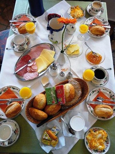 Ein reichhaltiges Frühstücksbuffet mit Brötchen, Käse, Wurst und Marmelade. Dazu gibt es frischen O-Saft und Kaffee in ansprechenden Tassen.