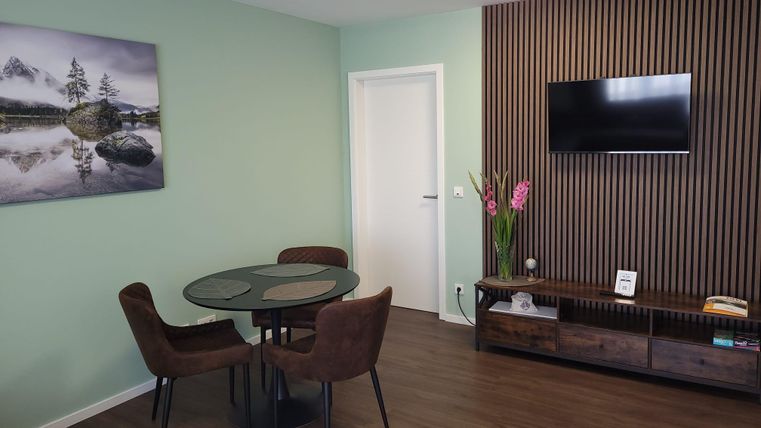 A modern living room with a round table, chairs, and a television. A picture of a landscape hangs on the wall.