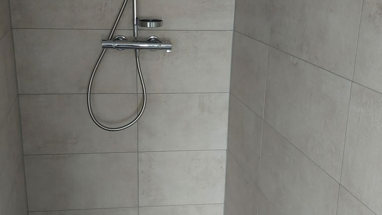 Een moderne douche met grijze tegels. De douchekop en de kraan zijn van roestvrij staal.