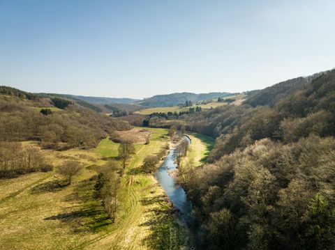 Landschaft mit Fluss, Wiesen und Hügeln unter blauem Himmel.