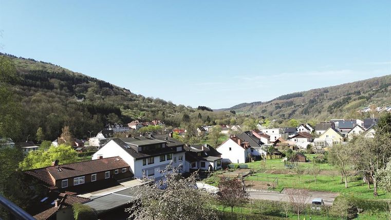 Eine malerische Landschaft mit einem kleinen Dorf am Fuße der Berge. Die Umgebung ist grün mit Wohnhäusern und einem klaren blauen Himmel.