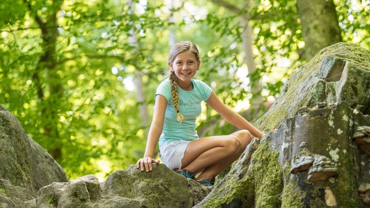 Mädchen sitzt auf einem moosbedeckten Felsen im Wald.