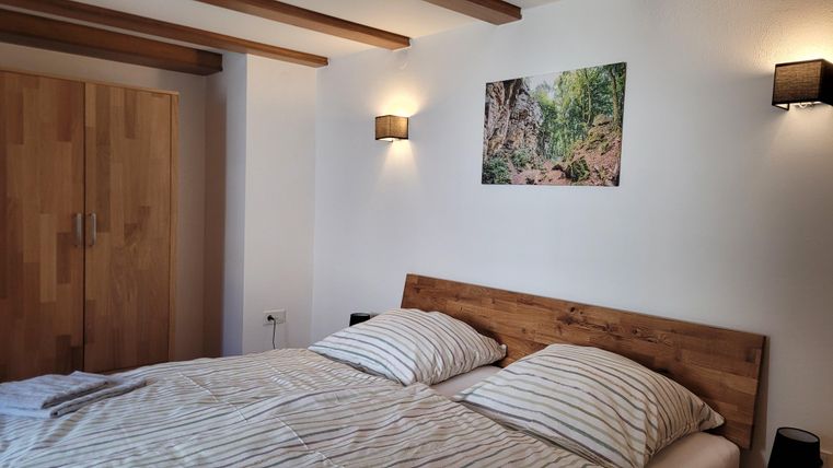 Ein gemütliches Schlafzimmer mit einem Doppelbett und gestreiften Bettlaken. An der Wand hängt ein Bild einer natürlichen Landschaft, und es gibt Holzschränke.