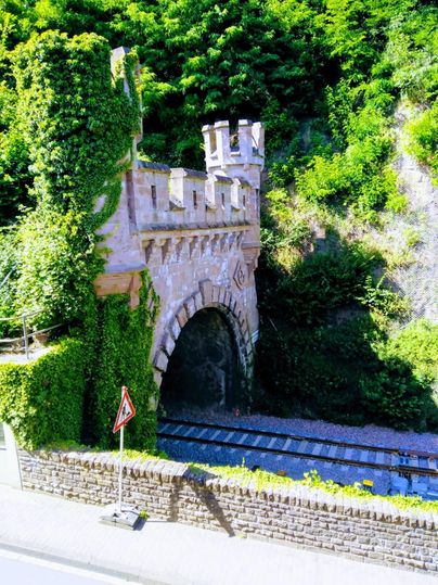 Un vieux pont avec des créneaux, couvert de plantes vertes. En dessous, une ligne de chemin de fer passe.