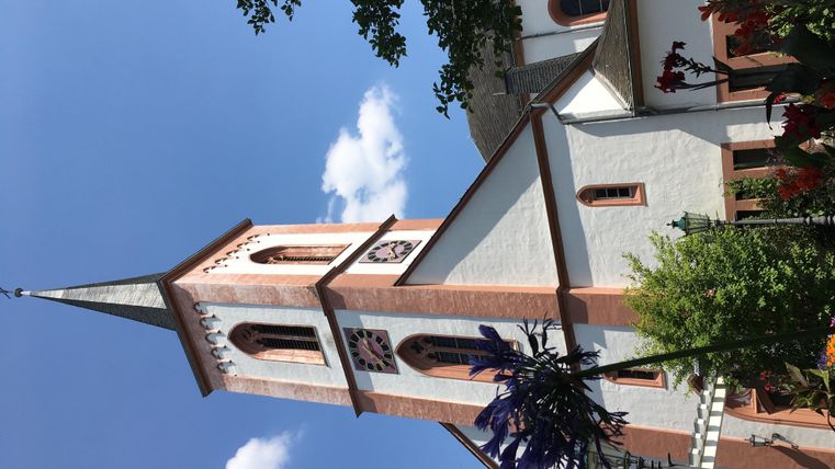 Eine charmante Kirche mit einem hohen Turm und schönen Details. Der Himmel ist blau mit wenigen Wolken.