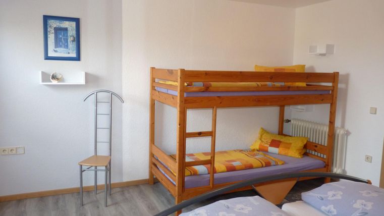 Ein einfaches Zimmer mit einem Etagenbett und zwei Einzelbetten. Die Wände sind hell und es gibt einen dekorativen Rahmen mit einem Bild.