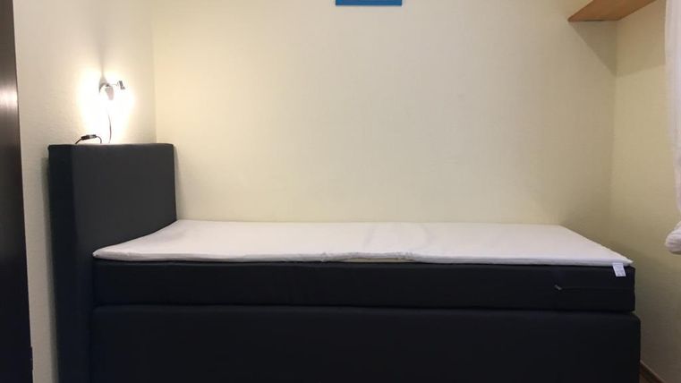 Une chambre simple avec un lit noir et une étagère murale. Un petit tableau est accroché au mur.