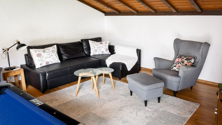 A cozy living area with a black couch and a gray armchair. The room has a wooden ceiling and a small table in the middle.