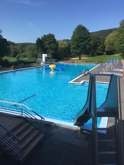 Een zwembad met helderblauw water en een glijbanengebied. Omgeven door bomen en een mooi landschap.