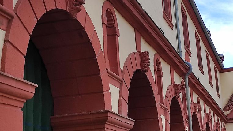 Een historisch gebouw met rode bogen en decoratieve steenhouwwerken. De gevel toont een combinatie van rode en lichte kleurtinten.