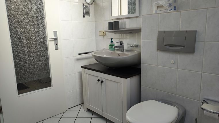 Ein modernes Badezimmer mit einem Waschbecken und einem WC. Die Wände sind gefliest und es gibt einen großen Spiegel.