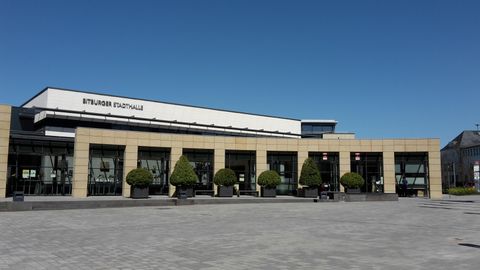 Ein modernes Gebäude mit großen Fenstern und einem klaren blauen Himmel. Der Außenbereich hat gepflegte Pflanzen und einen ebenerdigen Platz.
