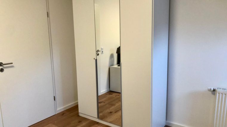 A bright room with a white mirrored cabinet and wooden floor. There is a radiator on one wall.