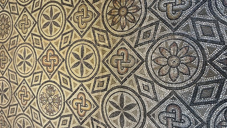 Ein eleganter Mosaikboden mit verschiedenen geometrischen Mustern und floralen Motiven. Die Farben sind in neutralen Tönen gehalten, was dem Design einen klassischen Look verleiht.