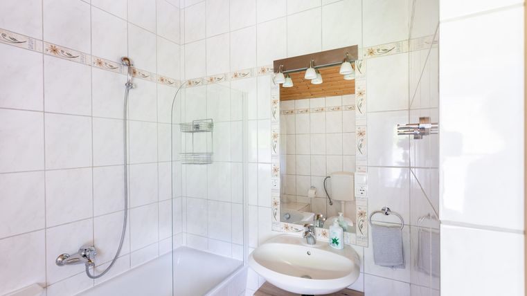 A bright bathroom with a bathtub and a sink. The walls are tiled and there is a large mirror over the sink.