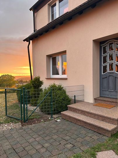 Een charmant huis met een entree en een tuinhekje. Op de achtergrond is een mooie zonsondergang te zien.