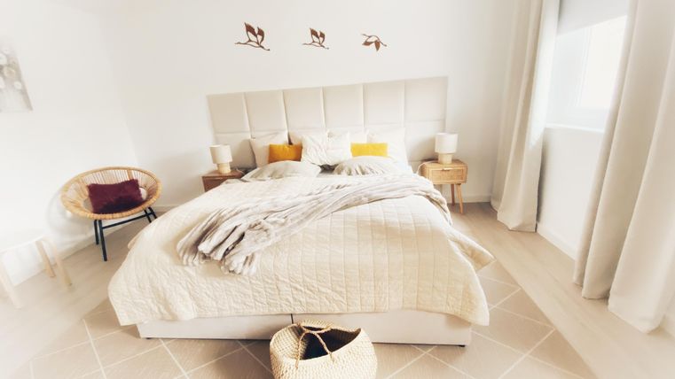 Ein helles Schlafzimmer mit einem bequemen Bett und gemütlicher Dekoration. Die Wände sind weiß und es gibt einige dekorative Elemente, die eine einladende Atmosphäre schaffen.