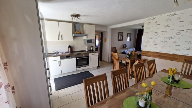 A modern kitchen with bright furniture and a dining table. The decoration is friendly and inviting.