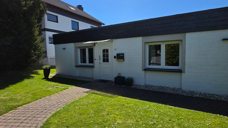 Ein modernes Haus mit einem grünen Rasen und einem gepflasterten Weg. Der Himmel ist klar und blau.