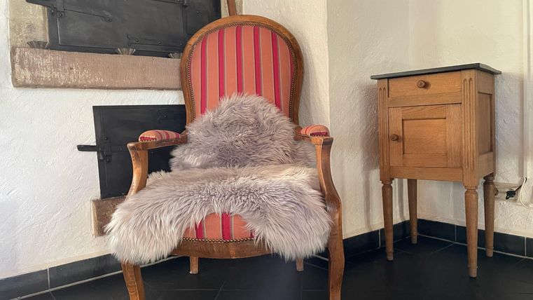 Un fauteuil confortable avec des rayures rouges et un jeté en fourrure se trouve dans une pièce. À côté du fauteuil se trouve une petite armoire en bois.