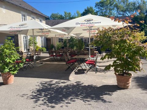 Un espace extérieur confortable avec des tables et des chaises sous de grands parasols. Entouré de plantes, cet endroit offre une impression accueillante pour les invités.