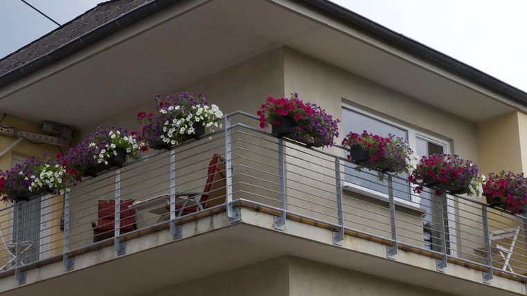 Ein schöner Balkon mit bunten Blumenkästen. Darauf stehen zwei Stühle und ein kleiner Tisch.