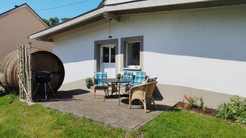 Een gezellig terras met een tafel en stoelen. Op de achtergrond staat een groot houten vat en een barbecue.