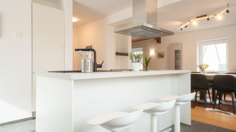 Une cuisine moderne avec un îlot de cuisine blanc et de hauts sièges. La pièce est lumineuse et accueillante, avec un coin repas à l'arrière.