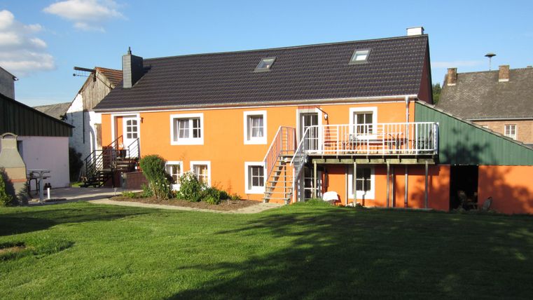 A colorful building with an orange facade and a garden. There is a terrace and some windows on the front.