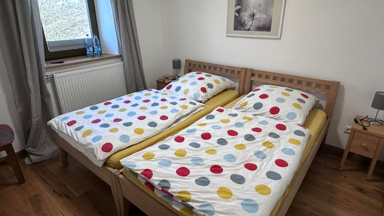 Ein gemütliches Schlafzimmer mit zwei Betten und bunten Bettüberzügen. Der Raum hat eine Fensteransicht und eine einfache, moderne Einrichtung.