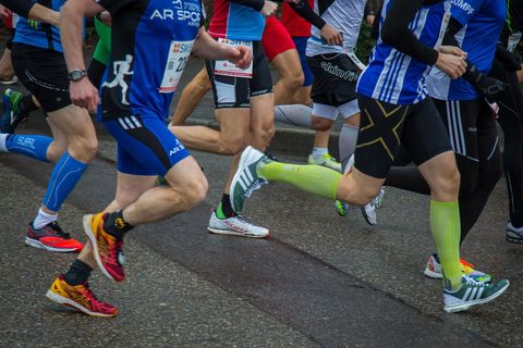 Eine Gruppe von Läufern in Sportkleidung bewegt sich schnell auf der Straße. Die Füße und Beine der Teilnehmer sind deutlich sichtbar, während sie an einem Wettlauf teilnehmen.