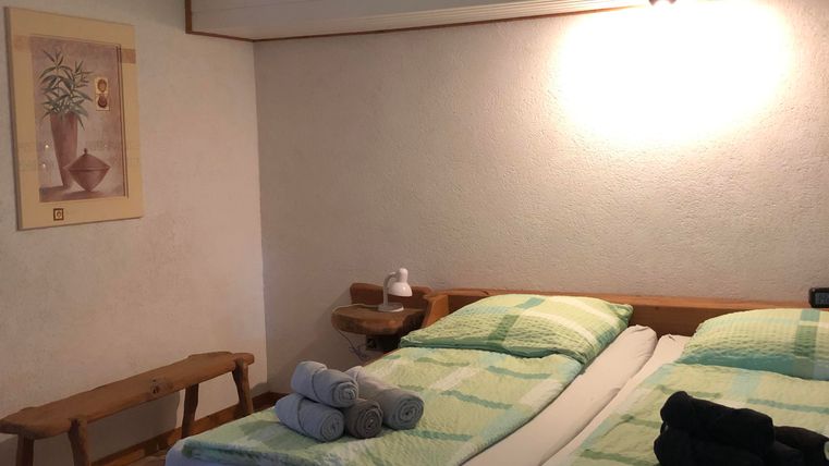 Une chambre confortable avec un lit double et une literie moderne. Un banc en bois, un plafonnier avec ventilateur intégré et une œuvre d'art complètent la décoration.