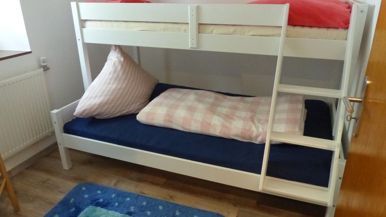 Un lit superposé avec un cadre blanc et une literie colorée. La pièce a un aspect lumineux et accueillant.