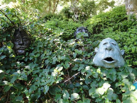 Gesichter aus Stein sind in dichtem Grün versteckt. Sie scheinen aus der Hecke zu schauen und verleihen der Szene eine mystische Atmosphäre.