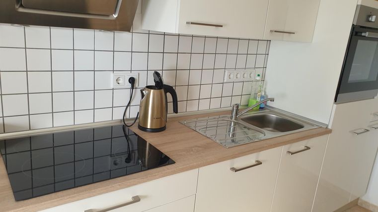 Une cuisine moderne avec des meubles blancs et une cafetière en acier inoxydable. La cuisinière est équipée d'une plaque de cuisson lisse et les murs sont carrelés.