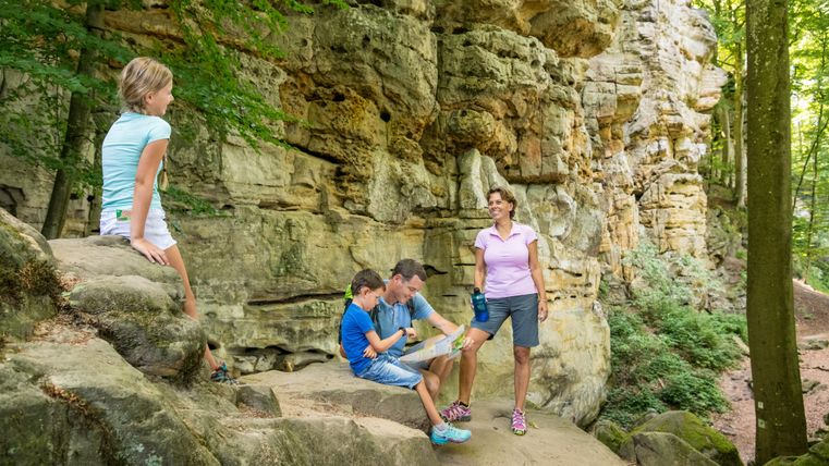 Familie macht Pause vor einer Felswand im Wald.