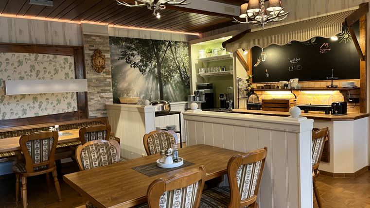 Ein gemütliches Café mit Holzmöbeln und einem warmen, einladenden Ambiente. Die Wand ist dekoriert mit einem großen Naturmotiv und die Theke ist gut ausgestattet.